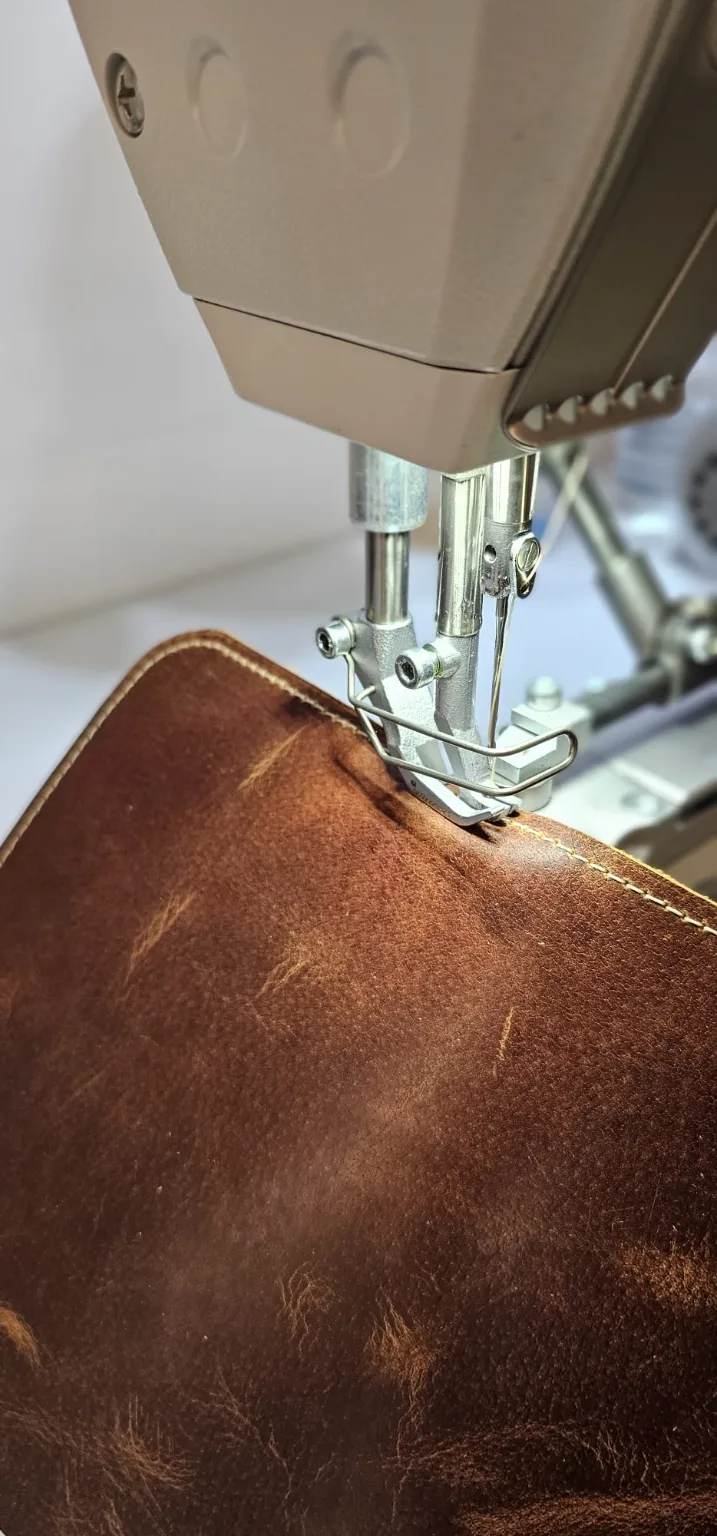 Couture du cuir à l'atelier R'Eve Couture d'une pièce en cuir marron sur une machine à coudre, à l'atelier R'Eve